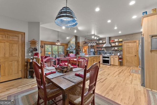 dining space with a ceiling fan, light wood-style floors, a fireplace, and vaulted ceiling