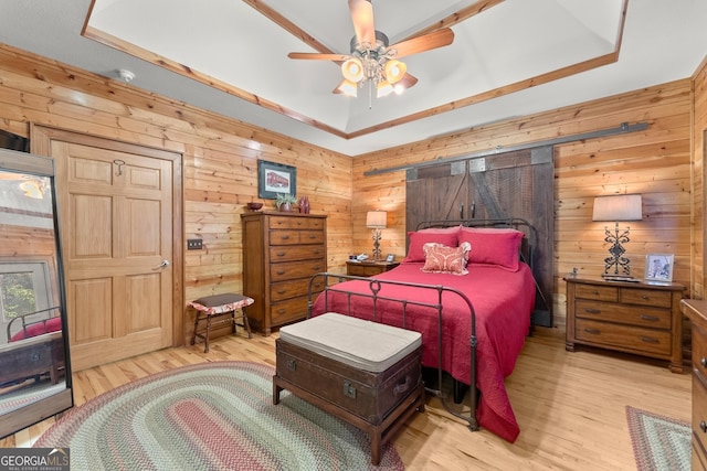 bedroom with a tray ceiling, wooden walls, and wood finished floors