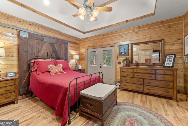 bedroom with wooden walls, french doors, a raised ceiling, and light wood-type flooring