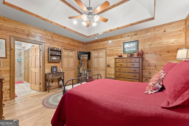 bedroom featuring a raised ceiling, wooden walls, wood finished floors, and ensuite bathroom