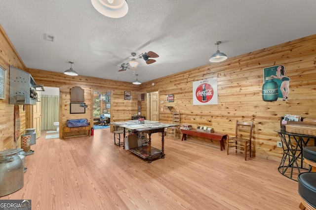 rec room with wooden walls, a textured ceiling, and hardwood / wood-style flooring