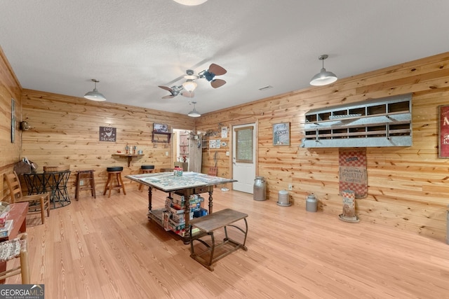 recreation room featuring ceiling fan, wood finished floors, wood walls, and a textured ceiling