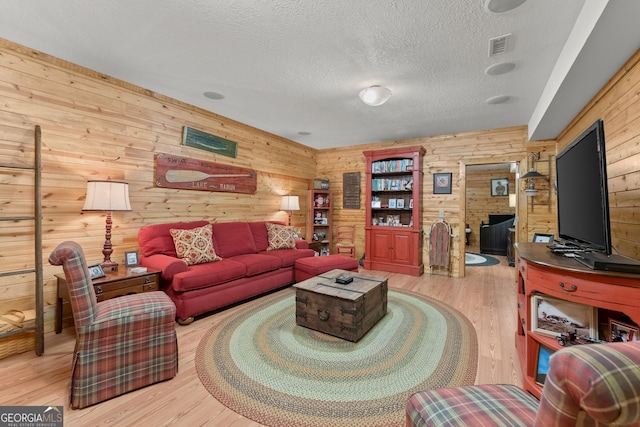 living room with wood walls, a textured ceiling, and light wood-type flooring