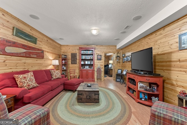 living room with visible vents, wood walls, a textured ceiling, and wood finished floors