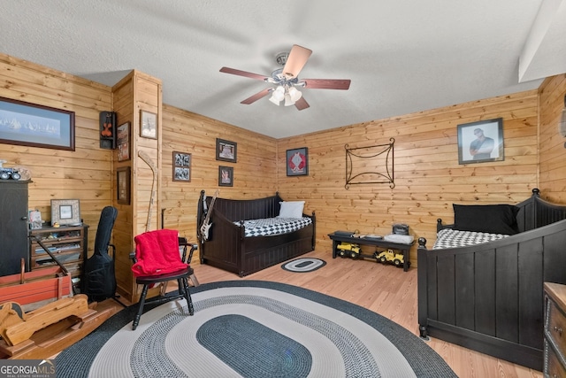 bedroom featuring wood walls, ceiling fan, light hardwood / wood-style floors, and a textured ceiling