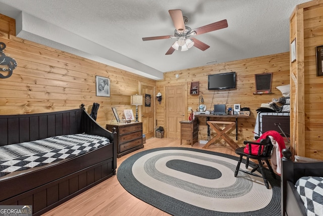 bedroom with ceiling fan, a textured ceiling, wooden walls, and light hardwood / wood-style flooring