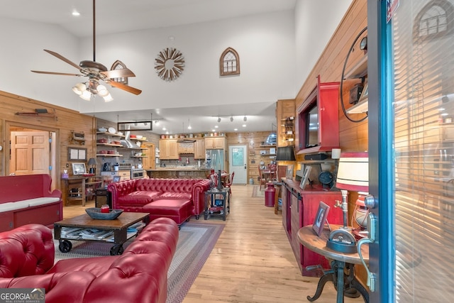 living room with a ceiling fan, light wood-type flooring, and wood walls