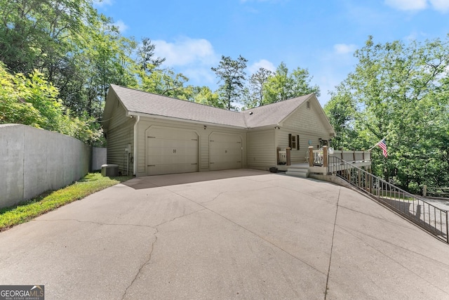 view of front facade with fence, central air condition unit, concrete driveway, roof with shingles, and an attached garage