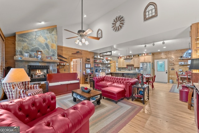 living area featuring ceiling fan, wood walls, a fireplace, light wood-style floors, and high vaulted ceiling