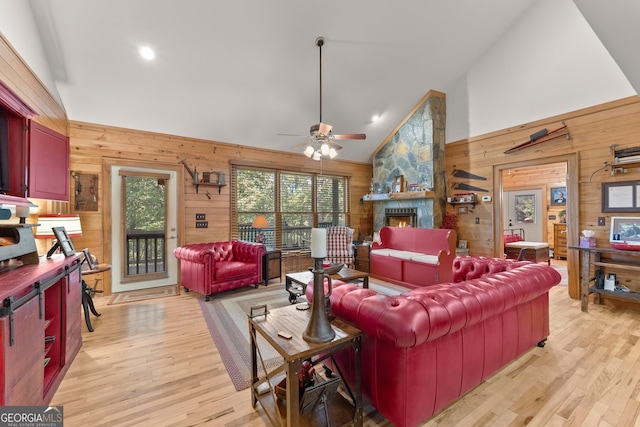 living room with wooden walls, a fireplace, high vaulted ceiling, and light wood-style floors