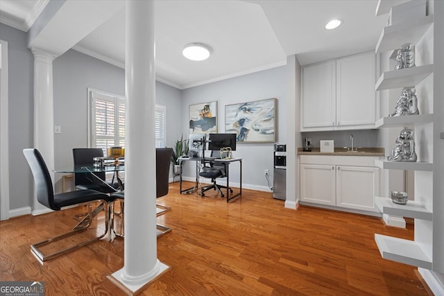 office with light hardwood / wood-style floors, crown molding, and decorative columns