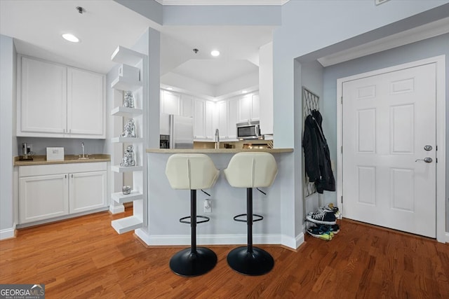 kitchen with appliances with stainless steel finishes, a kitchen bar, white cabinetry, and light hardwood / wood-style flooring