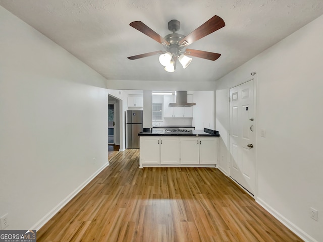 kitchen with ceiling fan, white cabinets, wall chimney exhaust hood, light hardwood / wood-style flooring, and stainless steel appliances