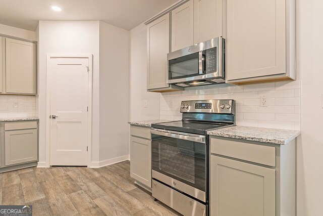 kitchen with appliances with stainless steel finishes, gray cabinetry, light wood-type flooring, and light stone counters