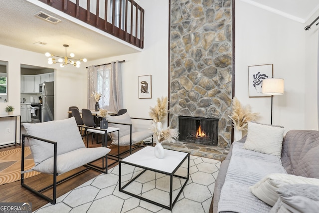 living room featuring a stone fireplace, a notable chandelier, light hardwood / wood-style floors, and a textured ceiling