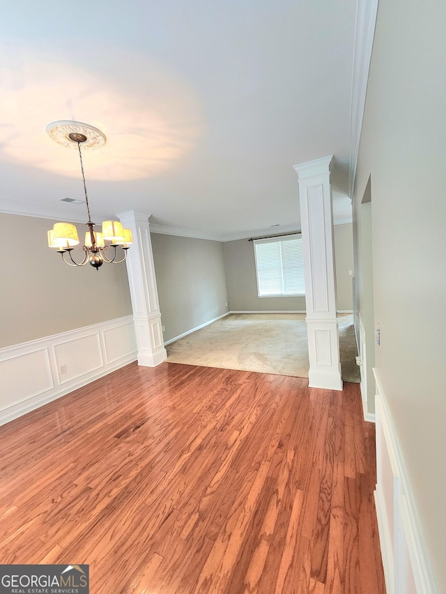 spare room with crown molding, light wood-style floors, decorative columns, and a notable chandelier