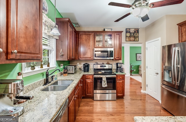 kitchen featuring appliances with stainless steel finishes, light hardwood / wood-style floors, light stone counters, ceiling fan, and sink