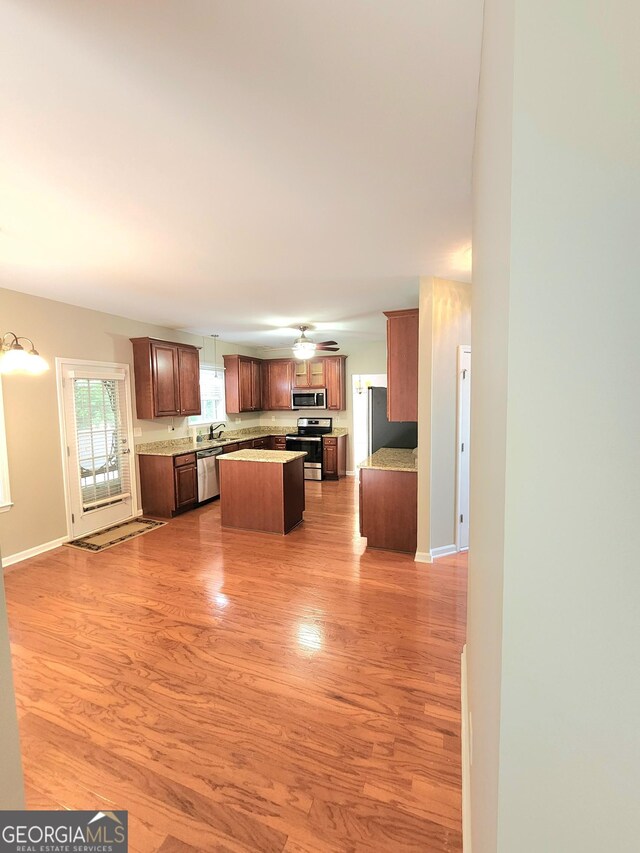 kitchen with a kitchen island, appliances with stainless steel finishes, light wood-type flooring, light countertops, and baseboards