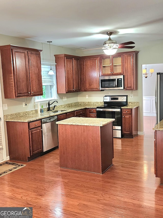 kitchen with ceiling fan, a sink, stainless steel appliances, wood finished floors, and pendant lighting
