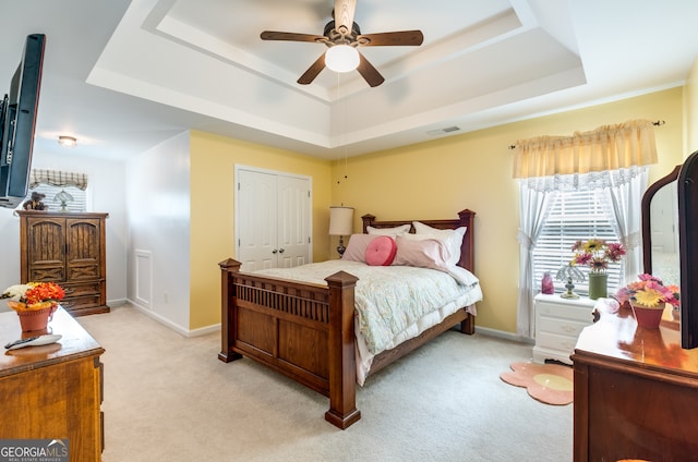 carpeted bedroom with a tray ceiling, ceiling fan, and a closet