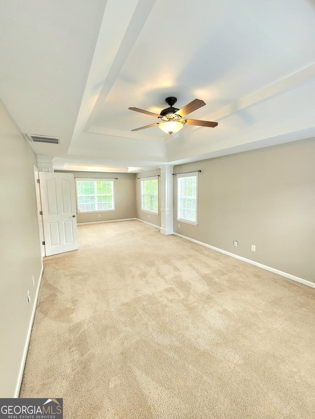 empty room featuring light carpet, a ceiling fan, baseboards, a tray ceiling, and visible vents