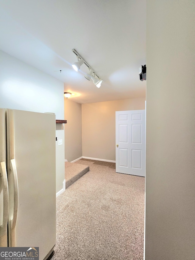 below grade area with freestanding refrigerator, rail lighting, carpet floors, and baseboards