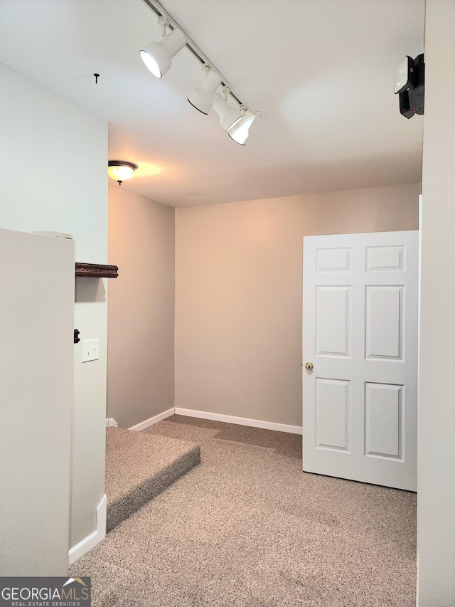empty room featuring carpet floors, baseboards, and track lighting