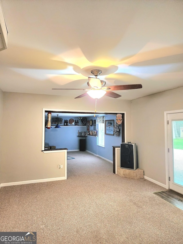 unfurnished living room featuring a ceiling fan, baseboards, and carpet