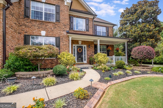 view of front of property with covered porch, a front lawn, and brick siding