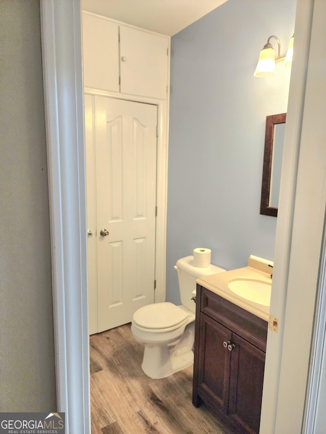 half bath featuring vanity, toilet, and wood finished floors