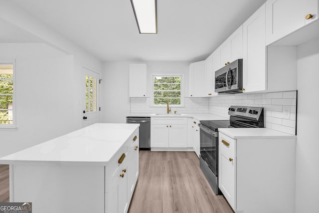 kitchen with white cabinets, sink, a kitchen island, stainless steel appliances, and light hardwood / wood-style floors