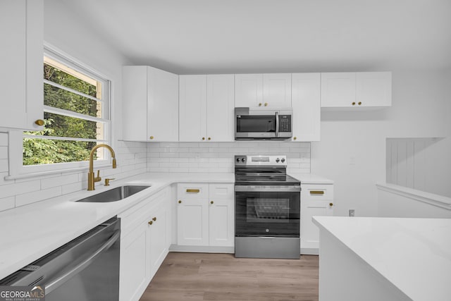 kitchen with sink, white cabinetry, stainless steel appliances, light wood-type flooring, and decorative backsplash