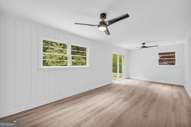 unfurnished living room with light hardwood / wood-style floors, wooden walls, and ceiling fan