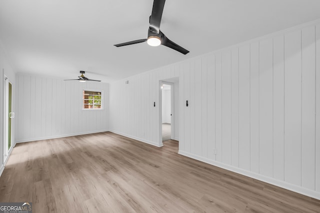 spare room with ceiling fan, light hardwood / wood-style flooring, and wood walls