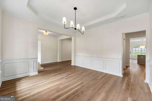 spare room featuring ornamental molding, a tray ceiling, a notable chandelier, and light hardwood / wood-style floors