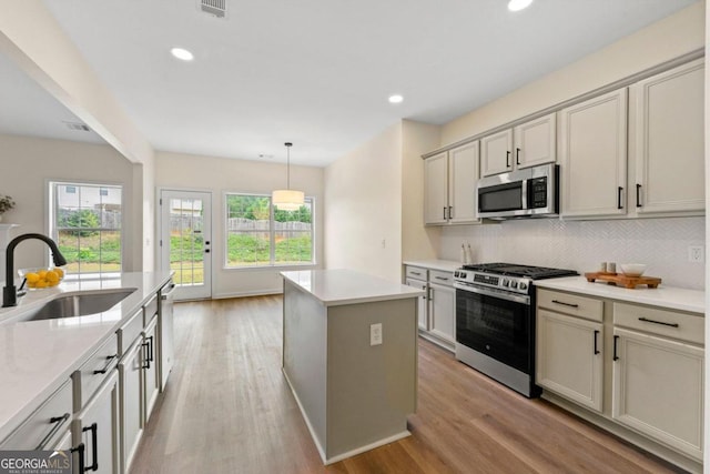 kitchen with tasteful backsplash, stainless steel appliances, sink, decorative light fixtures, and a kitchen island