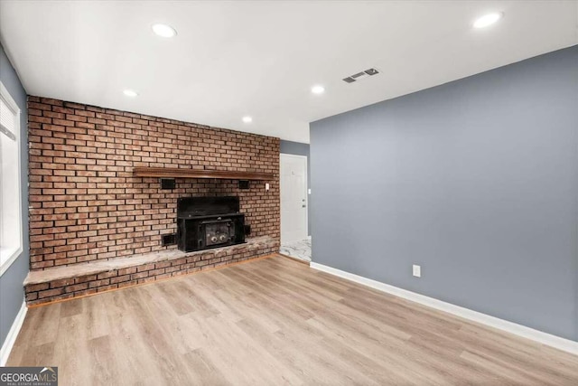 unfurnished living room with a brick fireplace, light hardwood / wood-style flooring, and brick wall