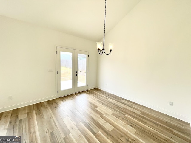 unfurnished dining area featuring french doors, a notable chandelier, light wood-style flooring, high vaulted ceiling, and baseboards