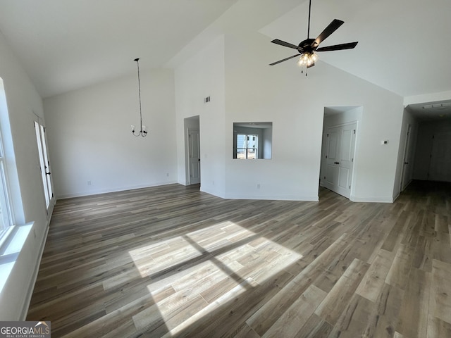 unfurnished living room featuring high vaulted ceiling, ceiling fan with notable chandelier, baseboards, and wood finished floors