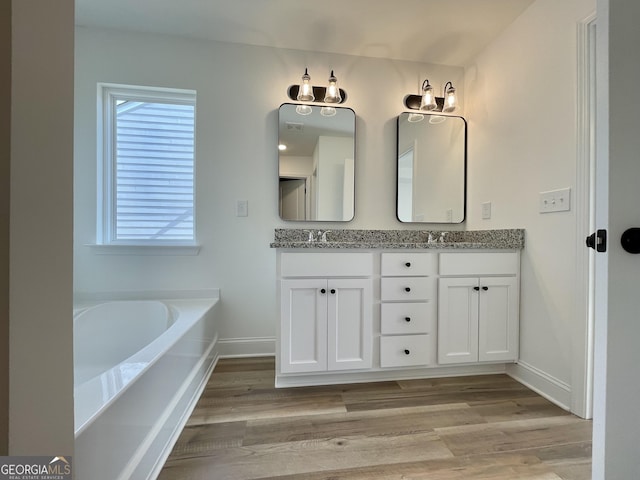 full bath with a sink, double vanity, wood finished floors, and baseboards