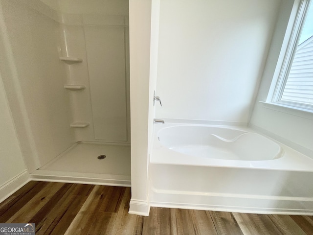 full bathroom with wood finished floors, a bath, and a shower stall