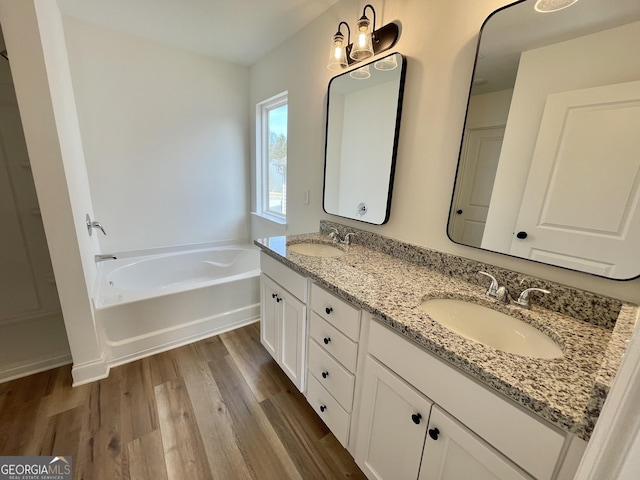 bathroom with double vanity, a garden tub, a sink, and wood finished floors