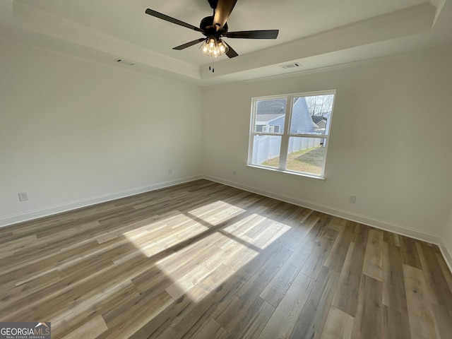 empty room with ceiling fan, wood finished floors, visible vents, baseboards, and a raised ceiling