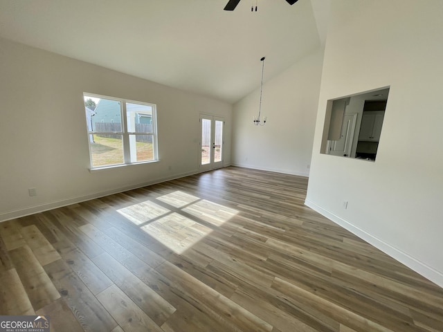 unfurnished living room featuring baseboards, ceiling fan, wood finished floors, french doors, and high vaulted ceiling