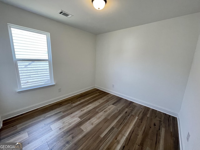 empty room with dark wood finished floors, visible vents, and baseboards