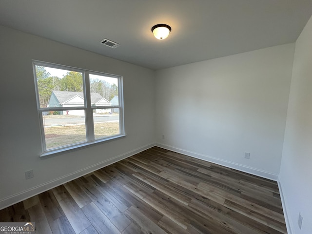 unfurnished room featuring dark wood-type flooring, visible vents, and baseboards