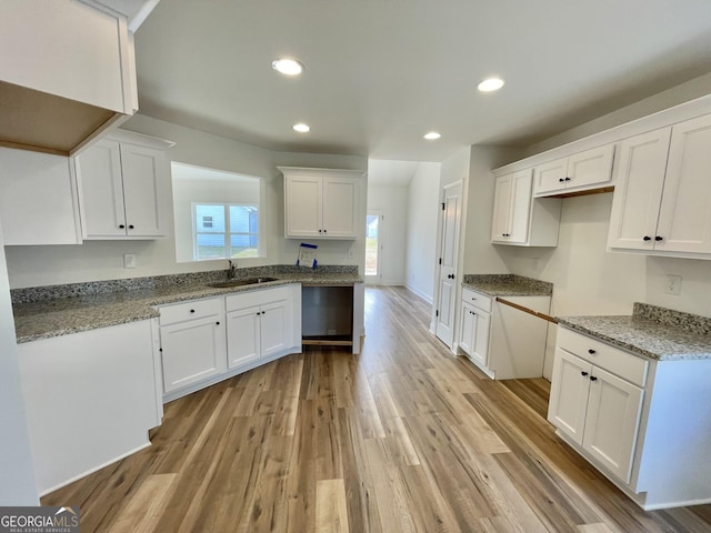 kitchen featuring light wood finished floors, stone countertops, white cabinets, a sink, and recessed lighting