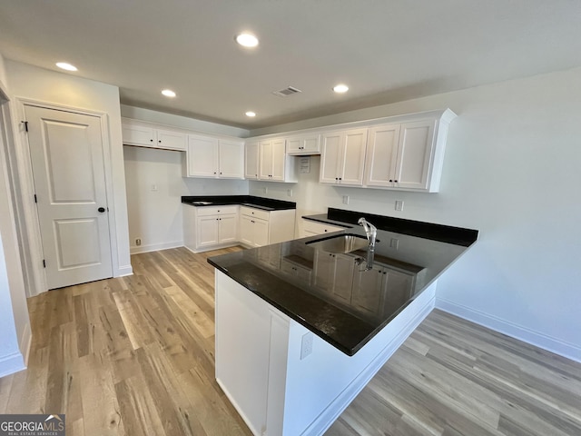 kitchen featuring dark countertops, white cabinetry, a sink, and light wood-style flooring