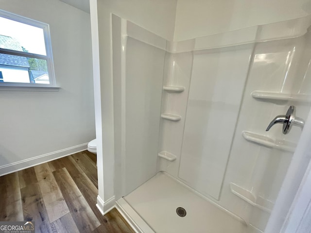 bathroom with a walk in shower, toilet, baseboards, and wood finished floors