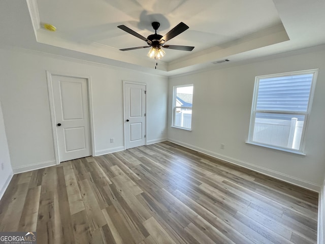 unfurnished bedroom with crown molding, a tray ceiling, visible vents, and light wood-style floors